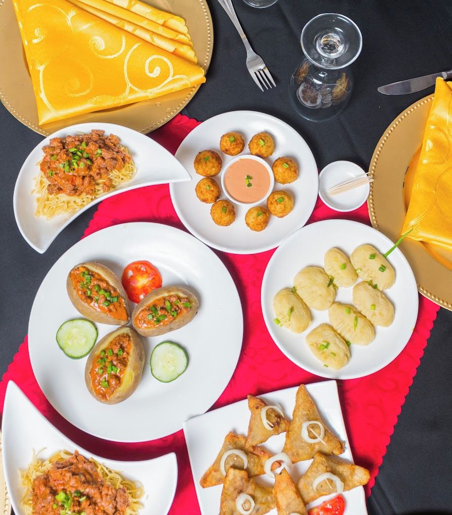 Uma mesa com diversos pratos, incluindo massa, dumplings e samosas.