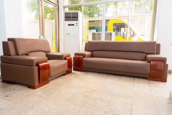 A room with two brown leather sofas and armchairs, a large window with a view of a yellow bus, and a white air conditioning unit.
