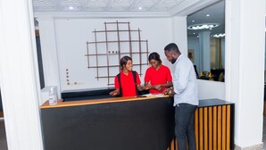 Un comptoir d’accueil au design moderne, avec un plan de travail en bois et une grille métallique décorative fixée au mur derrière.