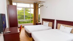 Une chambre d’hôtel avec deux lits, un bureau, une chaise et une grande fenêtre donnant sur un paysage verdoyant.