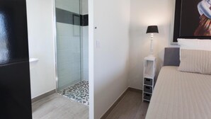 A hotel room with a bed, a nightstand with a lamp, a glass shower enclosure, and a tiled floor. - Spacious villa with pool and panoramic views (Aigne)