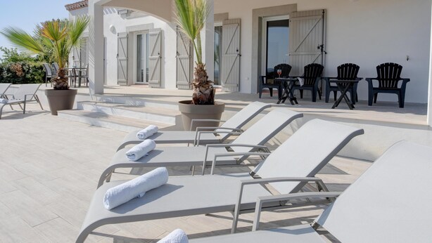 A sunlit outdoor lounge area with white lounge chairs, a table with chairs, and potted plants. - Spacious villa with pool and panoramic views (Aigne)