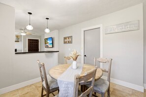 A dining area with a round table, chairs, a vase with dried flowers, pendant lights, and a wall-mounted sign.