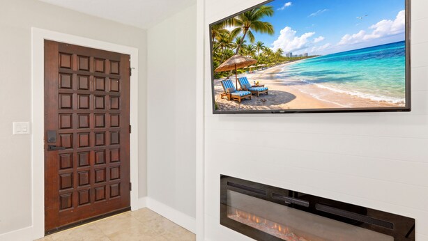 A room with a wooden door, a fireplace, and a TV displaying a beach scene. - Caloosahatchee Hideaway I, Waterfront Farmhouse Escape, Near Babcock Ranch (Fort Myers)