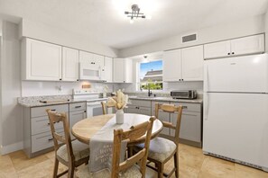 A modern kitchen with white cabinetry, a central island with chairs, a microwave, a toaster, and a refrigerator.