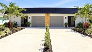 A modern building with a garage, a concrete driveway, and a row of plants on either side. - Caloosahatchee Hideaway I, Waterfront Farmhouse Escape, Near Babcock Ranch (Fort Myers)