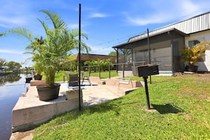 Un espace patio aménagé avec du mobilier d’extérieur, un barbecue et une vue sur un plan d’eau.