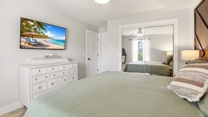 A bedroom with a bed, a dresser, a ceiling fan, a TV on the wall, and a door leading to another room. - Caloosahatchee Hideaway I, Waterfront Farmhouse Escape, Near Babcock Ranch (Fort Myers)
