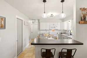 Une cuisine moderne avec des meubles blancs, un îlot central doté de tabourets, des luminaires suspendus et un four à micro-ondes.