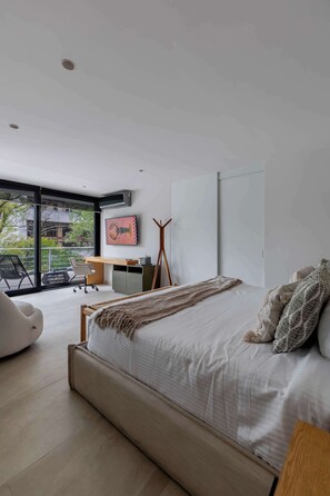 A modern bedroom with a large bed, a desk, and a view of the outdoors.