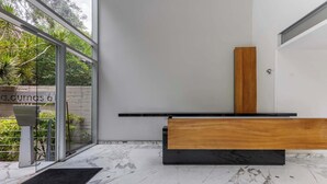 Um banheiro moderno com piso de mármore, um banco de madeira, bancada preta e porta de vidro que dá para um jardim.