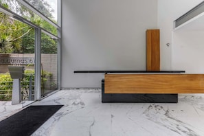A modern bathroom with a marble floor, a wooden bench, a black countertop, and a glass door leading to a garden. - Stunning Polanco 1BR Balcony & CDMX Views (Ciudad de México)