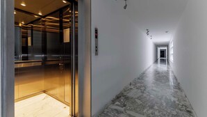 Um corredor com piso de mármore, um elevador e um painel digital.