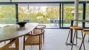 Uma área de refeições moderna com uma mesa grande, cadeiras de vime e vista para uma varanda através de amplas portas de vidro.