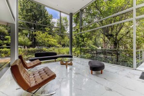 A modern interior with large windows, a glass table, leather seating, and a view of greenery outside. - Stunning Polanco 1BR Balcony & CDMX Views (Ciudad de México)