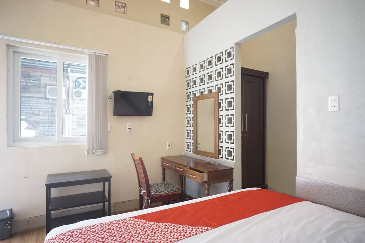 A bedroom with a bed, a desk, a chair, a television, and a window.