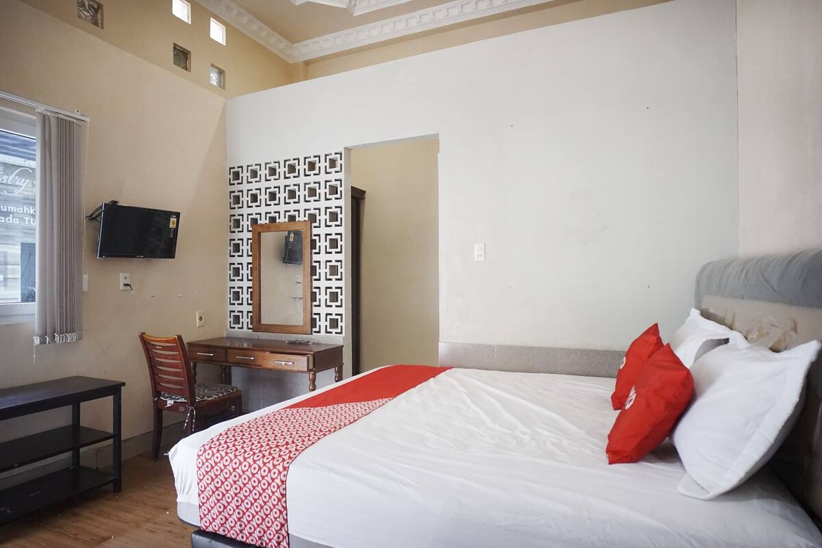 A hotel room with a bed, a desk, a chair, a TV, and a patterned wall.