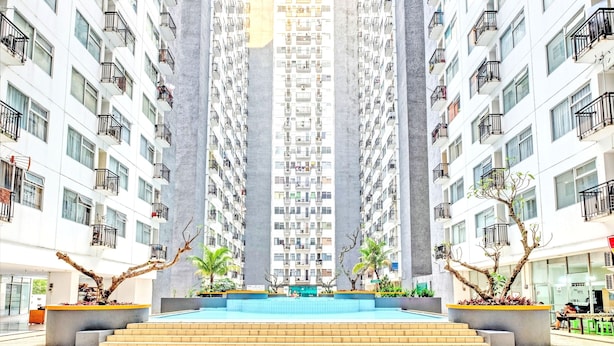 Un edificio residencial alto con balcones, un patio central con piscina y vegetación circundante.