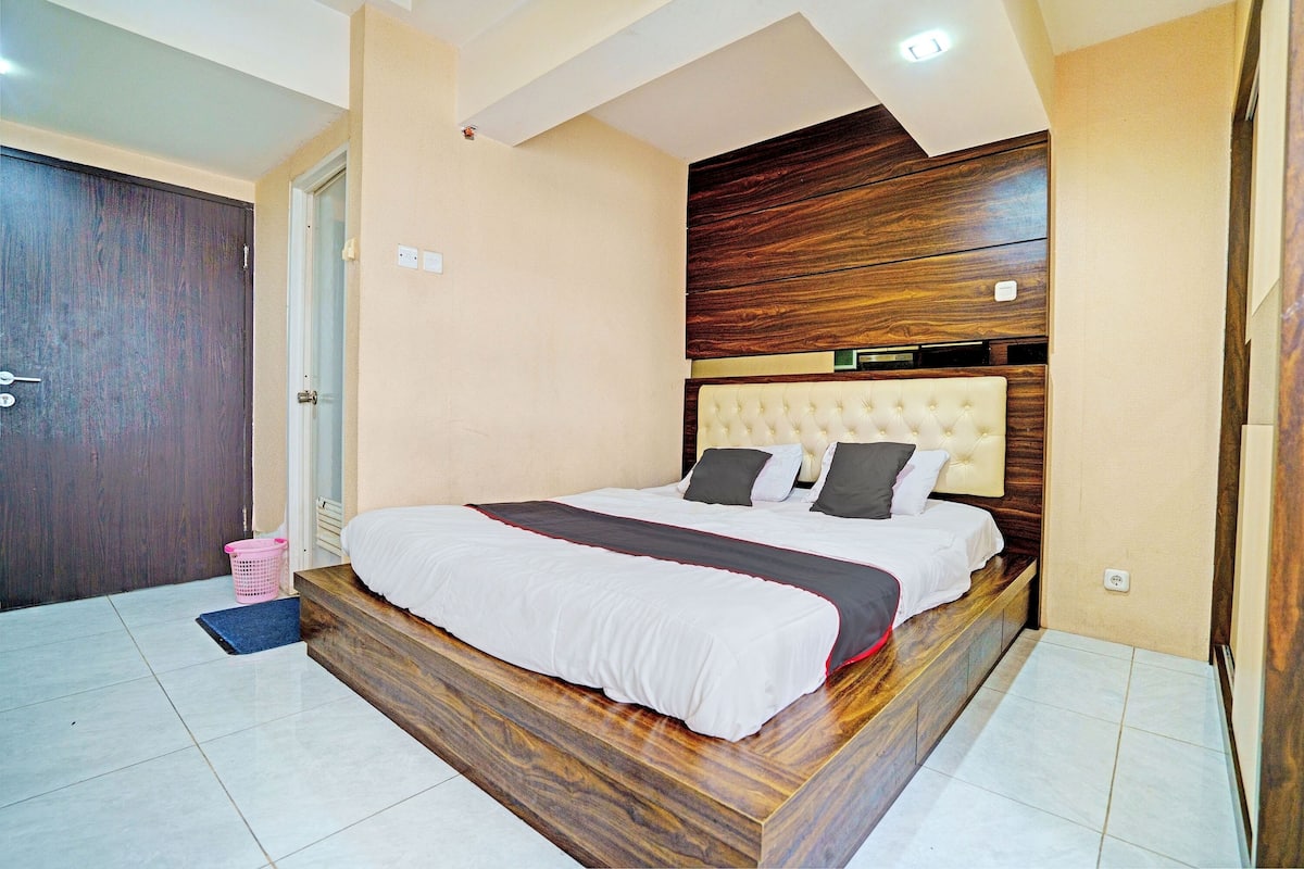 A bedroom with a wooden headboard, a large bed, a pink laundry basket, and a door.