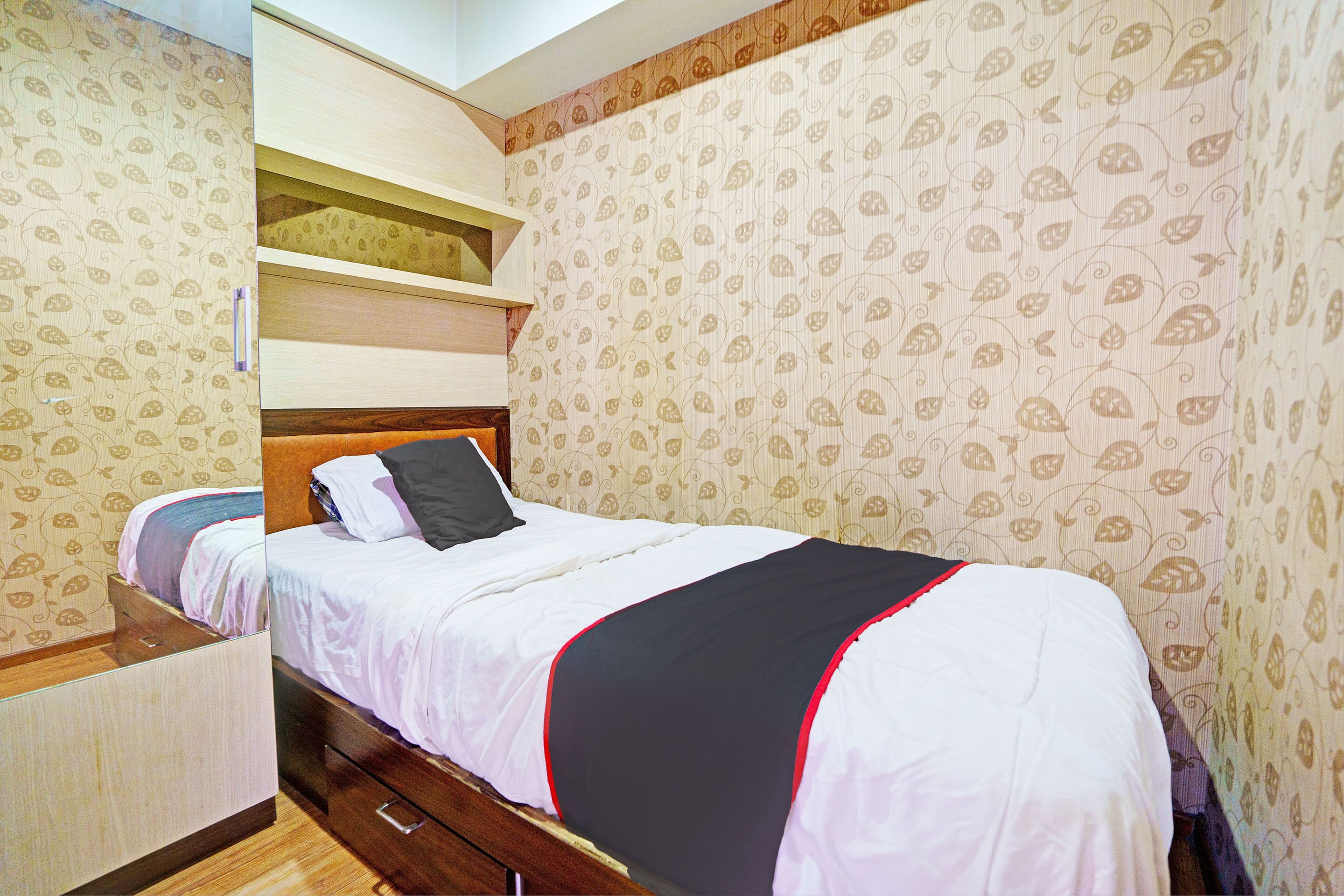 A bedroom with a bed, a wooden nightstand, a built-in shelf, and patterned wallpaper.