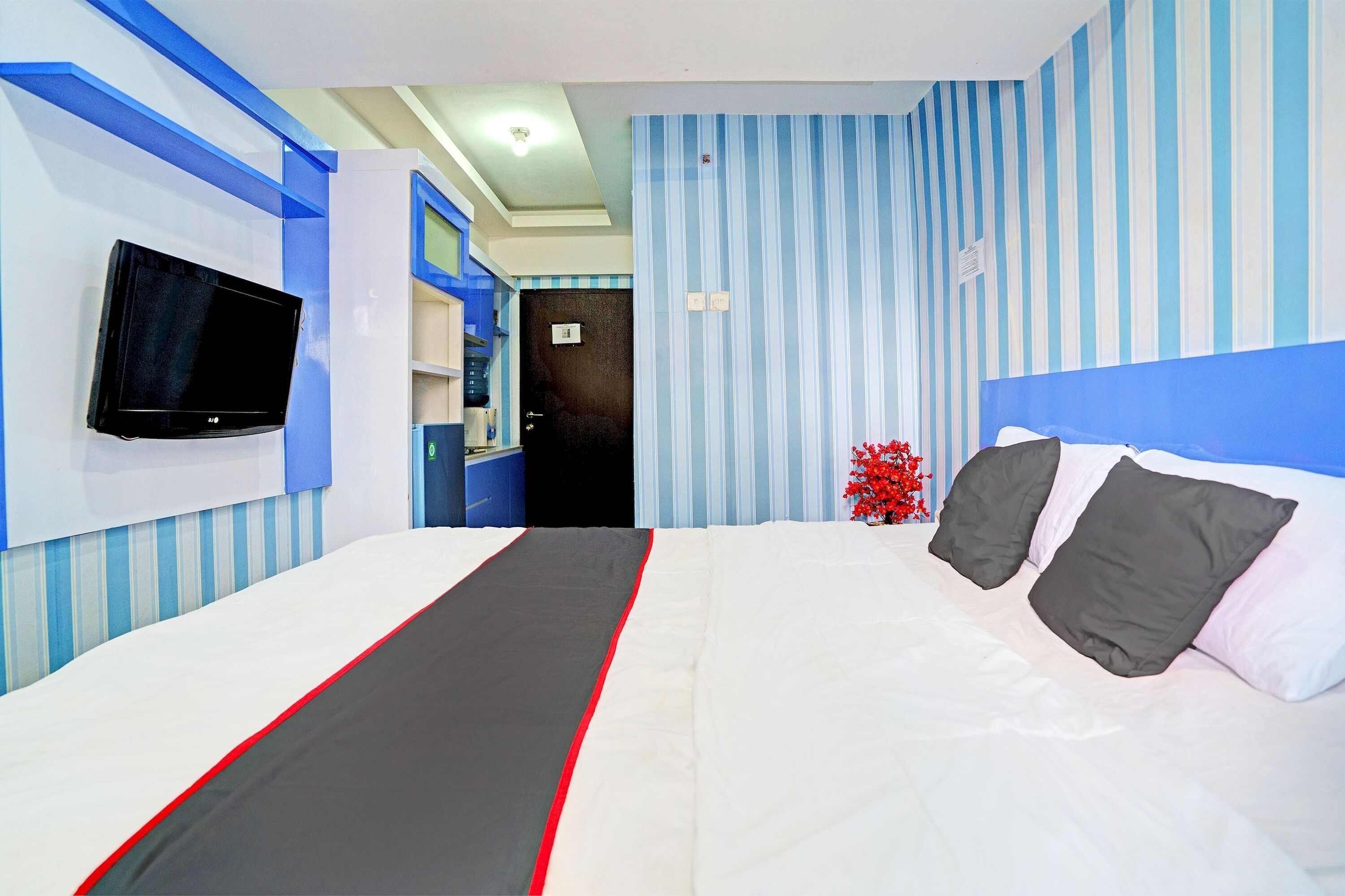 Una habitación de hotel con cama, televisión montada en la pared y papel tapiz a rayas.