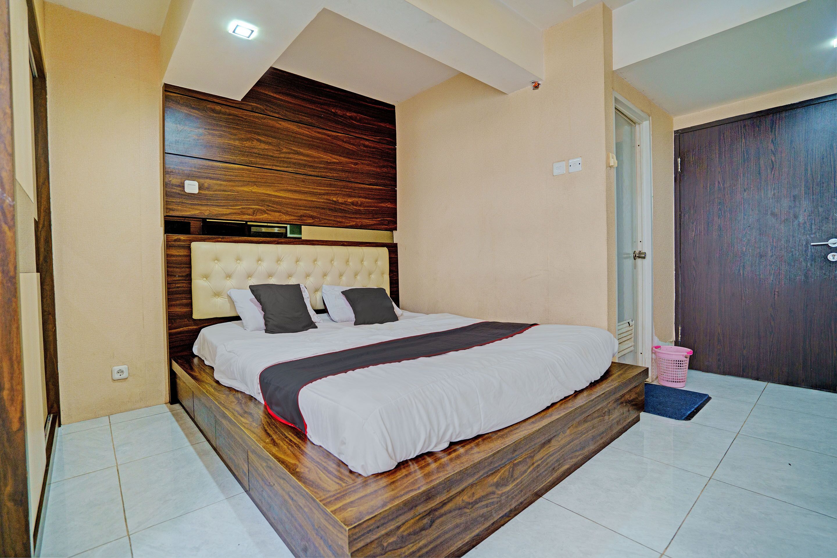 Een slaapkamer met een houten hoofdeinde, een bed met wit beddengoed en een roze wasmand.