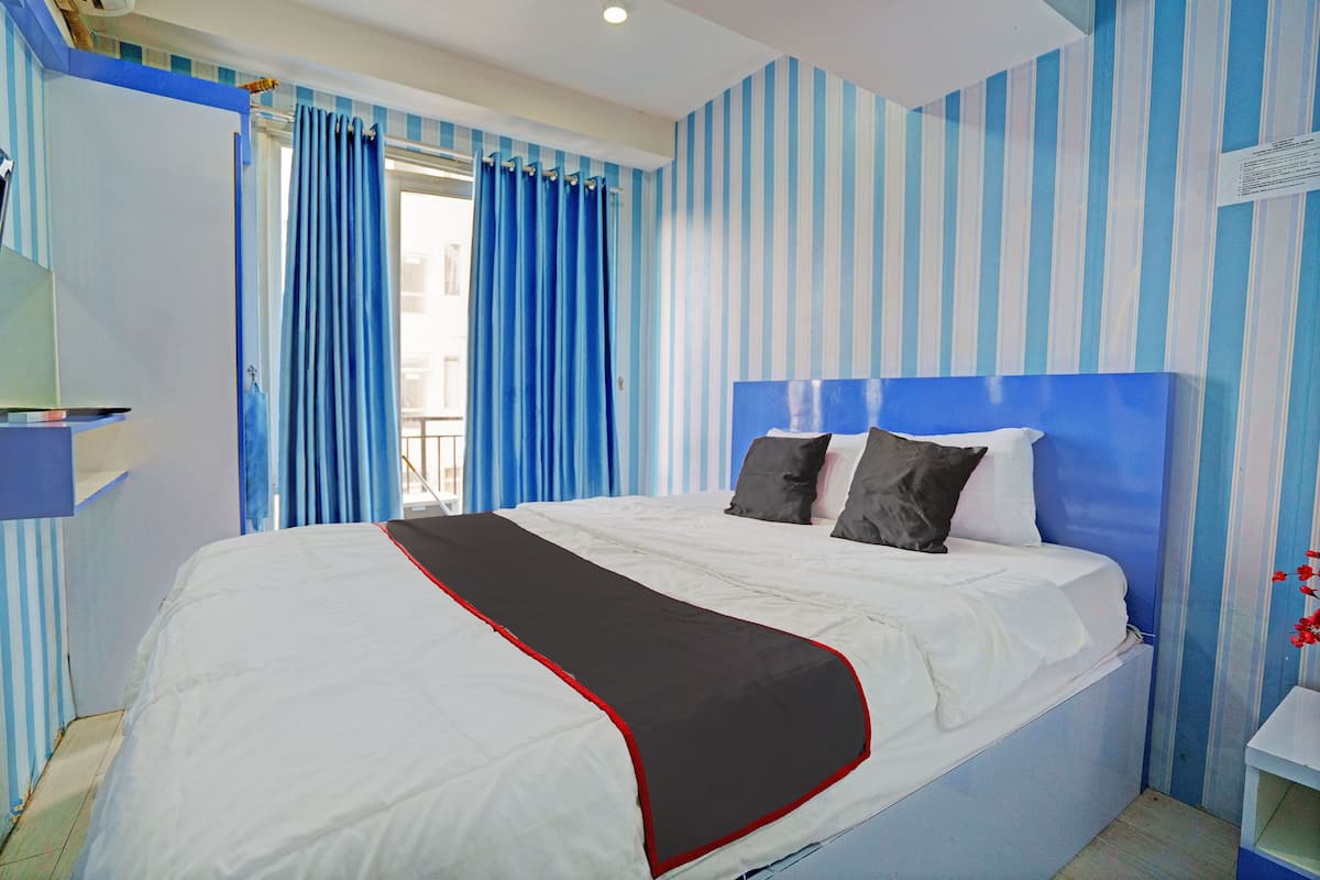 A bed with a white and red bedspread, a blue-striped wall, and a window with blue curtains.