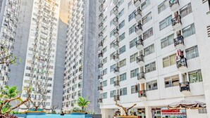 Un edificio residencial alto con balcones, una piscina y un pequeño espacio al aire libre con mesas y sillas.
