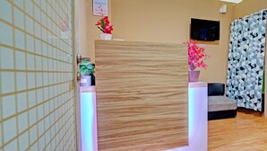 Un área de recepción con mostrador de madera, zona de estar, televisor en la pared y cortina estampada.