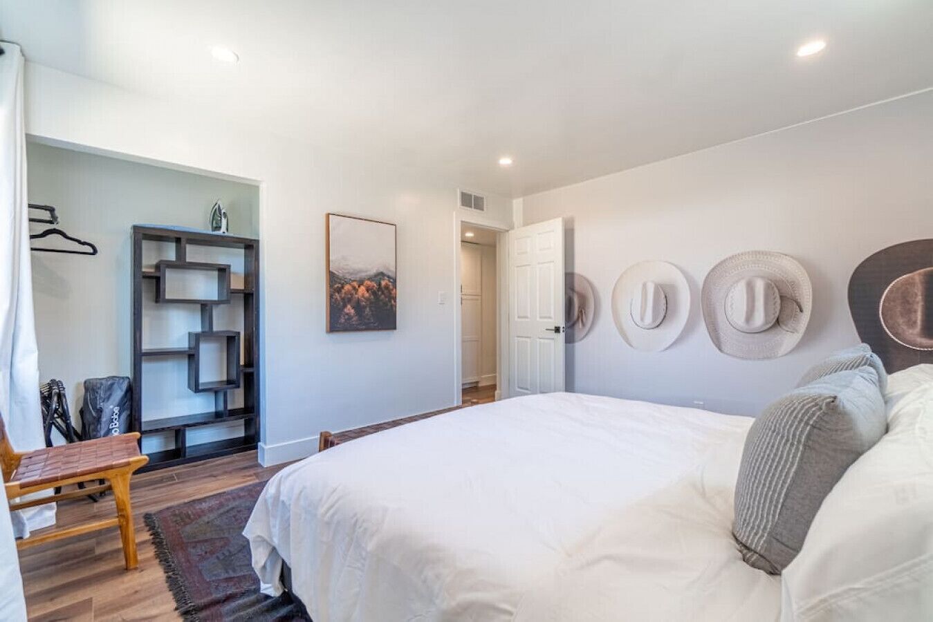 A bedroom with a large bed, a wooden chair, a wardrobe with a geometric design, and a wall-mounted hat display.