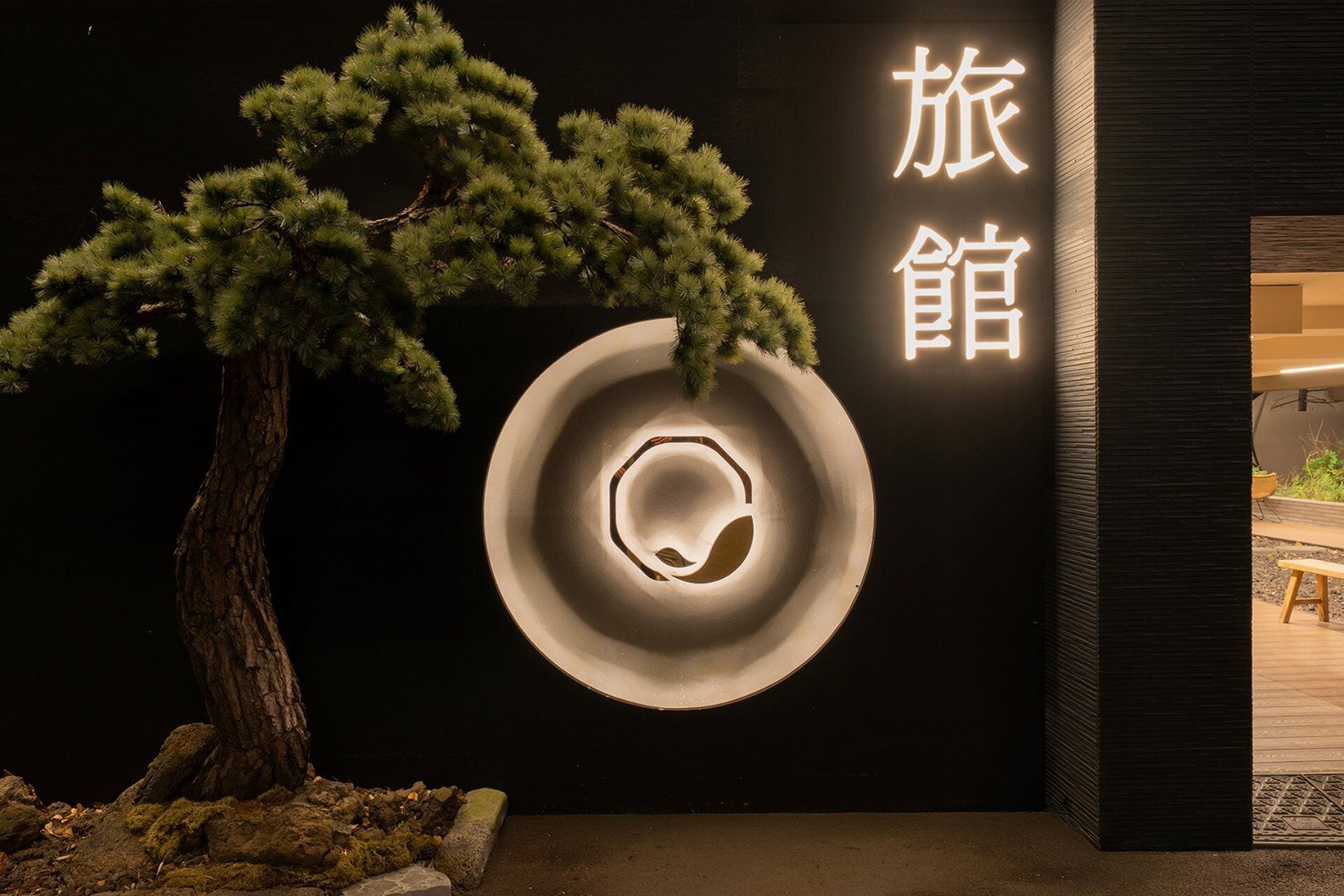 A minimalist interior with a bonsai tree, a circular wall design, and Japanese characters.