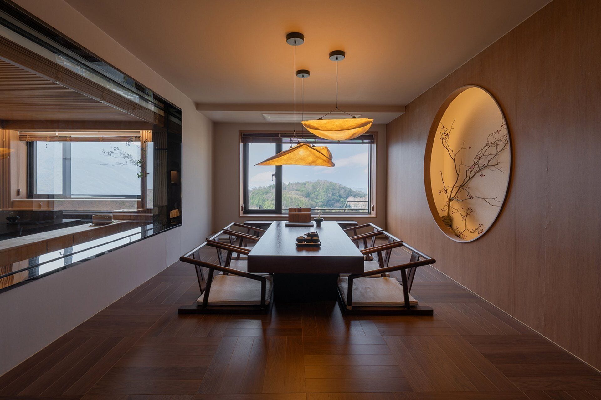 Un comedor moderno con una mesa larga, sillas, luces colgantes y un amplio ventanal con vistas.