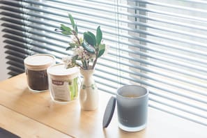 A table by the window features a vase with fresh flowers, a candle, and decorative containers.