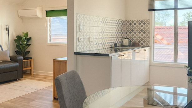 A modern kitchen with white cabinets, a glass dining table, and a blue rug. - Cosy and private self contained retreat in a great location, pet friendly (Graceville)