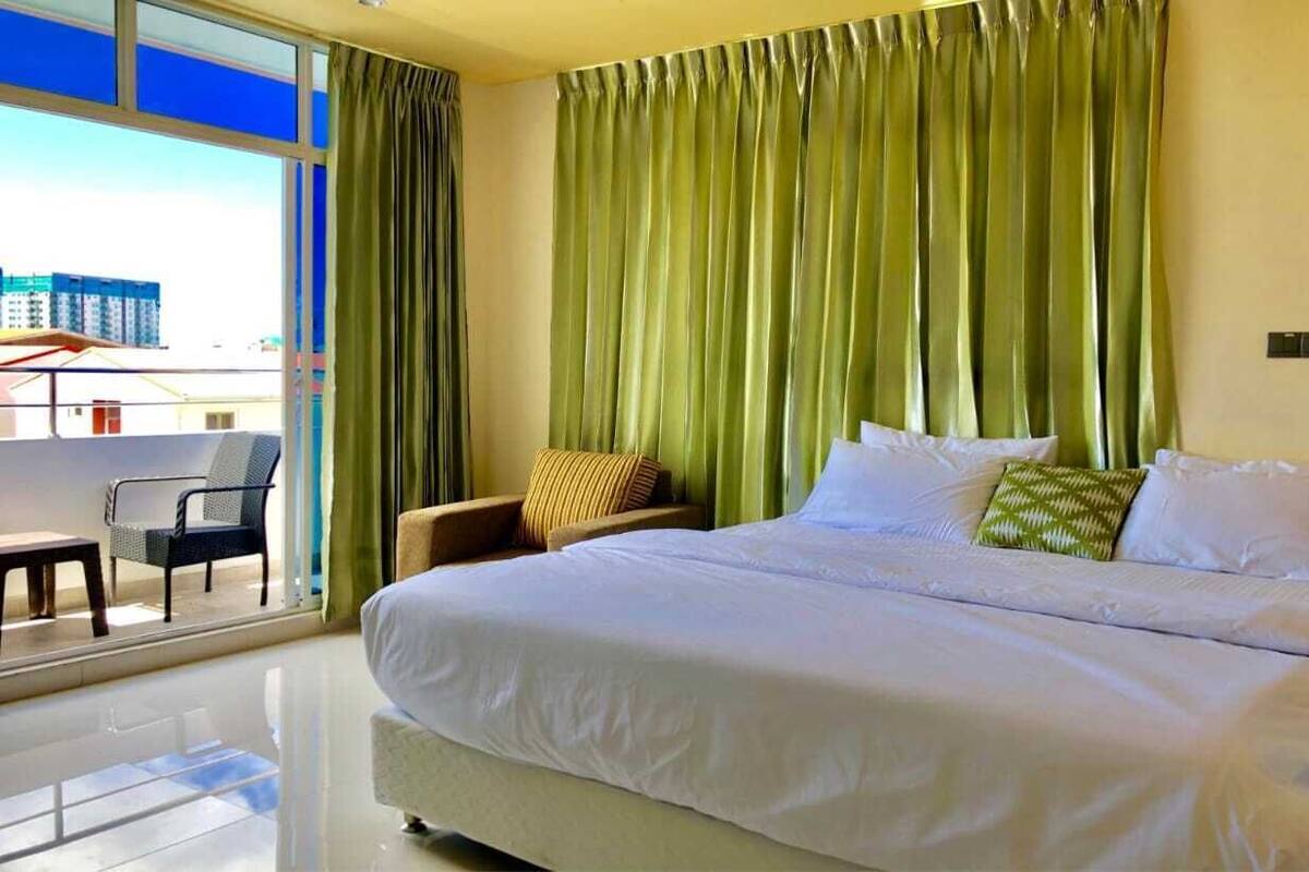 A hotel room with a large bed, a chair, a small table, and a view of buildings through a window.