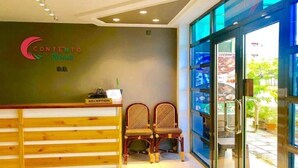 A reception area with a wooden counter, two wicker chairs, and a glass door leading outside. - Contento Retreat (Hulhumalé)