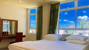 A hotel room with a large bed, a mirror, and two windows with curtains. - Contento Retreat (Hulhumalé)