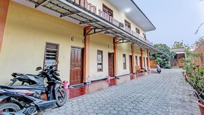 A building with a covered walkway, a parked scooter, and a potted plant. - SPOT ON 93007 Guest House Lestari (Prambanan)