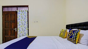 A bed with white bedding and a blue and yellow bed runner. There are two pillows with yellow and blue patterns. - SPOT ON 93007 Guest House Lestari (Prambanan)