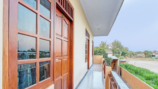 A corridor with large wooden doors and windows, a tiled floor, and a view of a residential area with greenery and houses. - SPOT ON 93007 Guest House Lestari (Prambanan)