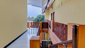 A corridor with a wooden bench, a tiled floor, and a view of a balcony with a railing. - SPOT ON 93007 Guest House Lestari (Prambanan)