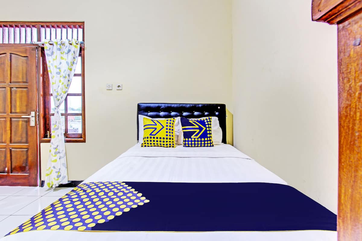 Une chambre à coucher avec un lit, deux oreillers, une couvre-lit bleue et jaune, une porte en bois et une fenêtre avec un rideau.