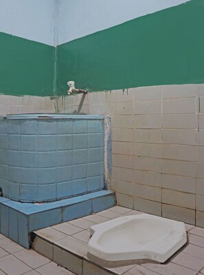 A small, basic bathroom with a blue water tank, a white toilet, and green and white tiled walls. - OYO 92994 Wisma Kencana Indah (Karehkel)