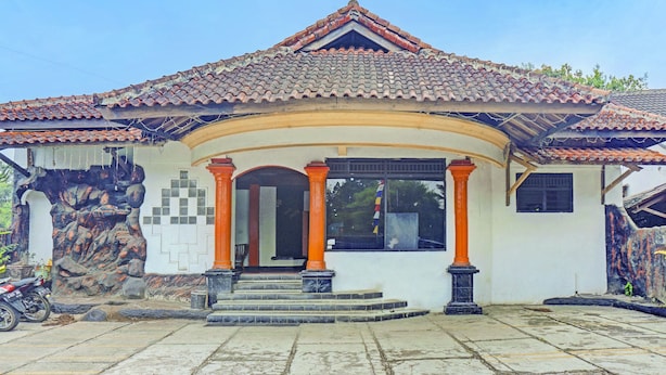 Um edifício com telhado de telhas, entrada central com degraus e um caminho de pedra que a conduz.