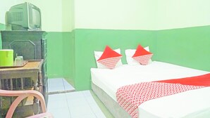 Um quarto com uma cama, uma televisão sobre um suporte e uma cadeira.