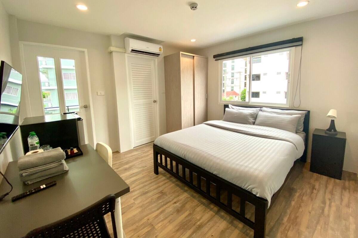 A hotel room with a bed, a desk, a chair, a TV, and a window with a view of buildings.