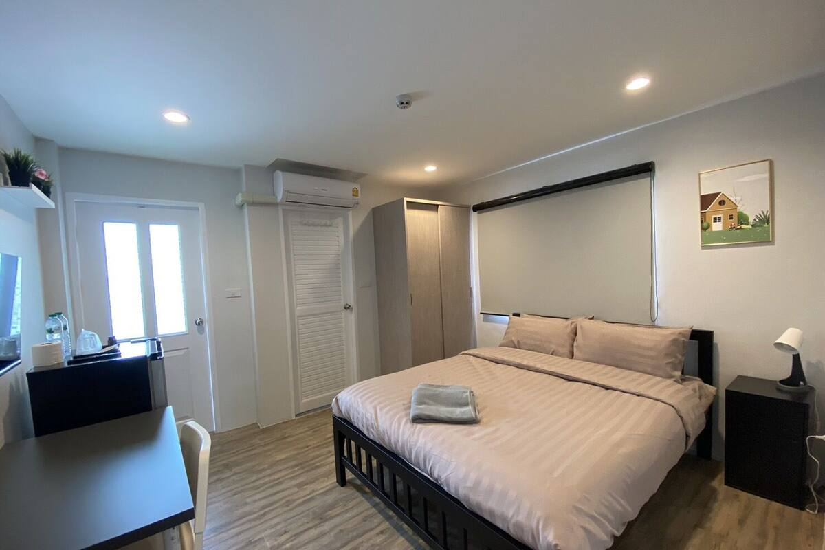 A bedroom with a bed, bedside table, desk, and a window.