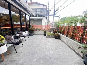 Eine Terrassenfläche mit Sitzgelegenheiten im Freien, Blumentöpfen und Blick auf die Straße.