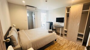 A hotel room with a bed, a desk, a TV, and a wardrobe. - Aree House Poshtel (Pattaya)