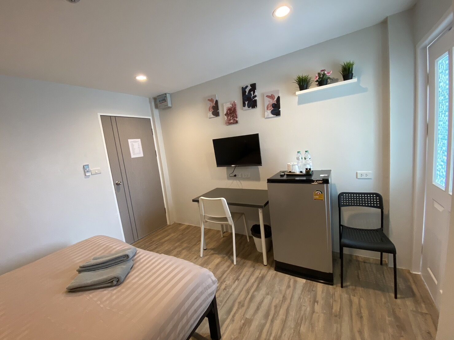 A compact hotel room with a bed, a desk with a chair, a television, a small refrigerator, and a window with a view.